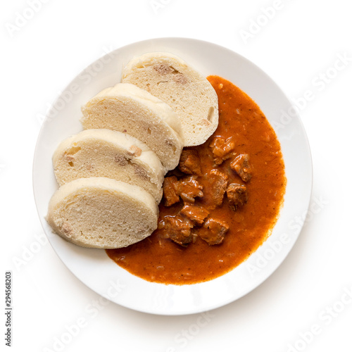 Beef goulash with bread dumplings on white ceramic plate isolated on white. Top view.