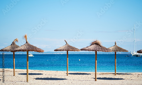 Idyllic scenery, concept of summer holidays, straw parasols in a row on the coast of blue Mediterranean Sea, Majorca Island, Baleares, Spain