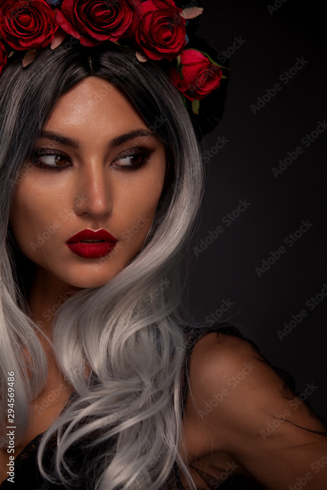 Creative image of Halloween makeup look or Dia De Los Muertos holiday on dark background with copyspace. Blonde model wearing a hat with red rose Creative image of Halloween makeup look or Dia De Los Muertos holiday on dark background with copyspace. Blonde model wearing a hat with red rose