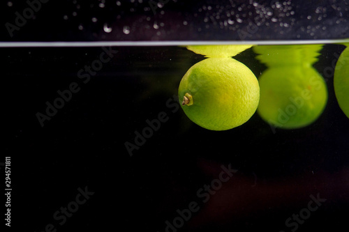 Green limes in water on a black background. © andrew_shots