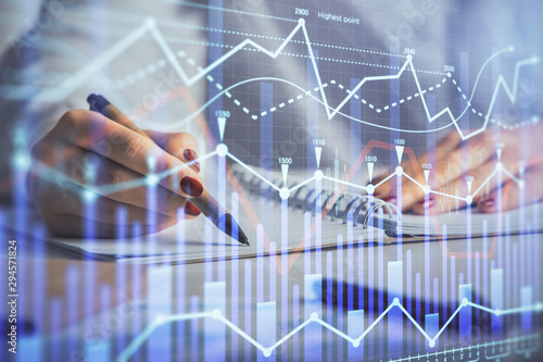 Double exposure of woman's hands making notes with forex graph hologram. Concept stock market analysis.