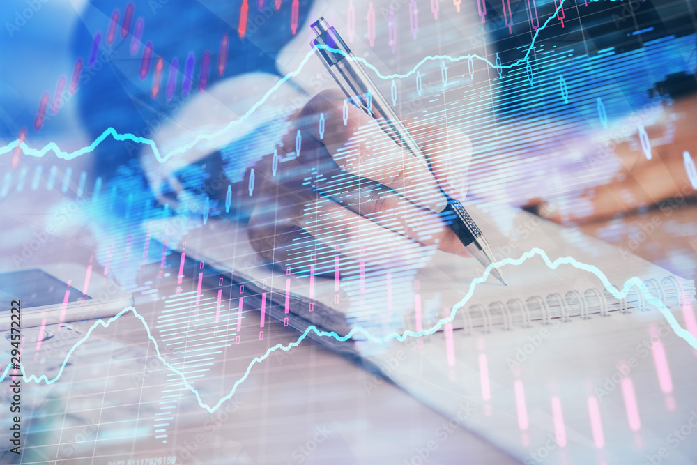 Obraz premium A woman hands writing information about stock market in notepad. Forex chart holograms in front. Concept of research. Multi exposure