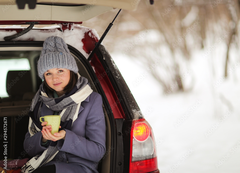 Caucasian woman with hot mug in the car trunk