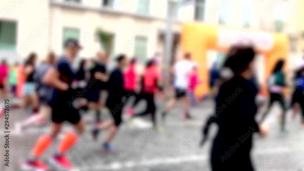 Closeup view of many blurry silhouettes of people running outdoors by city streets during charity City Marathon. Participants athletes run a long distance through the streets of the city. Slo-mo. Closeup view of many blurry silhouettes of people running outdoors by city streets during charity City Marathon. Participants athletes run a long distance through the streets of the city. Slo-mo.