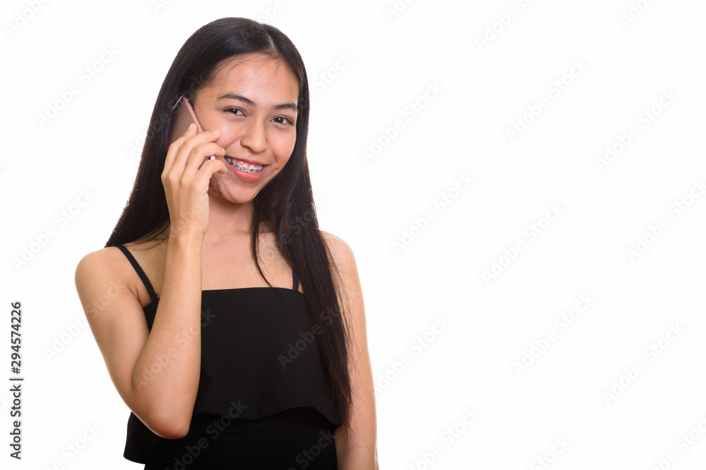 Young happy Asian teenage girl smiling while talking on mobile p Young happy Asian teenage girl smiling while talking on mobile p