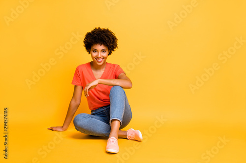 Portrait of positive charming cheerful girl sit have free time enjoy rest relax weekends wear casual style clothes sneakers isolated over yellow bright color background