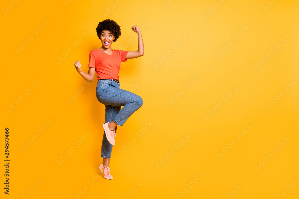 Copyspace photo of cheerful charming cute nice curly pretty sweet attractive girlfriend black skinned wearing jeans denim t-shirt footwear rejoicing isolated over yellow color background