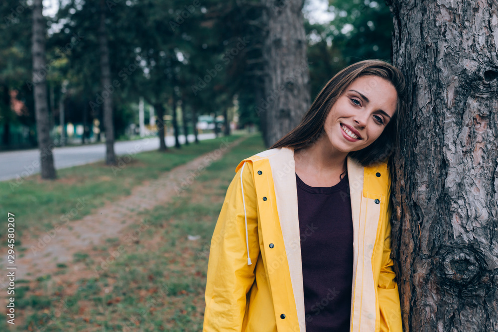 young woman in raincoat posing in park leaned on tree young woman in raincoat posing in park leaned on tree