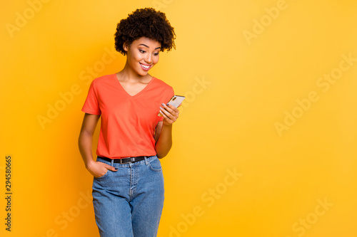Copyspace photo of beautiful cheerful cute charming gorgeous girlfriend standing confidently wearing t-shirt jeans denim holding phone isolated over yellow color vivid background