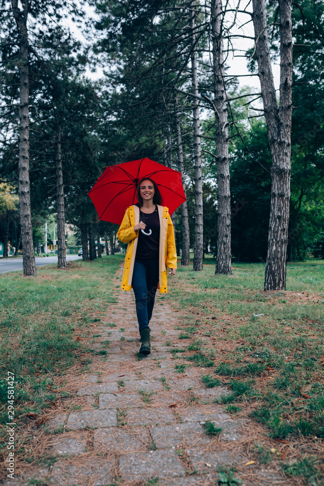 young woman in yellow raincoat with red umbrella in park young woman in yellow raincoat with red umbrella in park