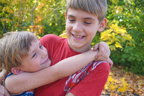 Cuadro en lienzo The younger brother hugs the older one and looks at him, two loving brothers are standing in an embrace in the park against the background of autumn leaves