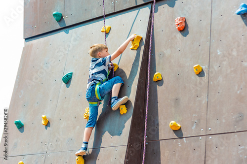A boy in climbing equipment conquers the top of an artificial tower for climbers in a sports extreme recreation park.