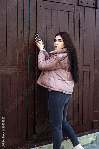 Young cute pregnant girl in pink warm down jacket trying to open the key lock. Late autumn, the cold is coming. toned photo. Very big door