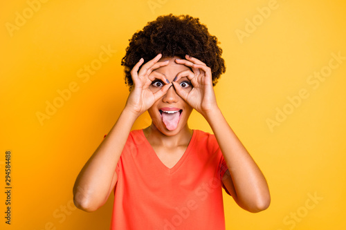 Photo of fooling cheerful funny cute nice attractive black girlfriend sticking her tongue out wearing orange t-shirt isolated over yellow vivid color background