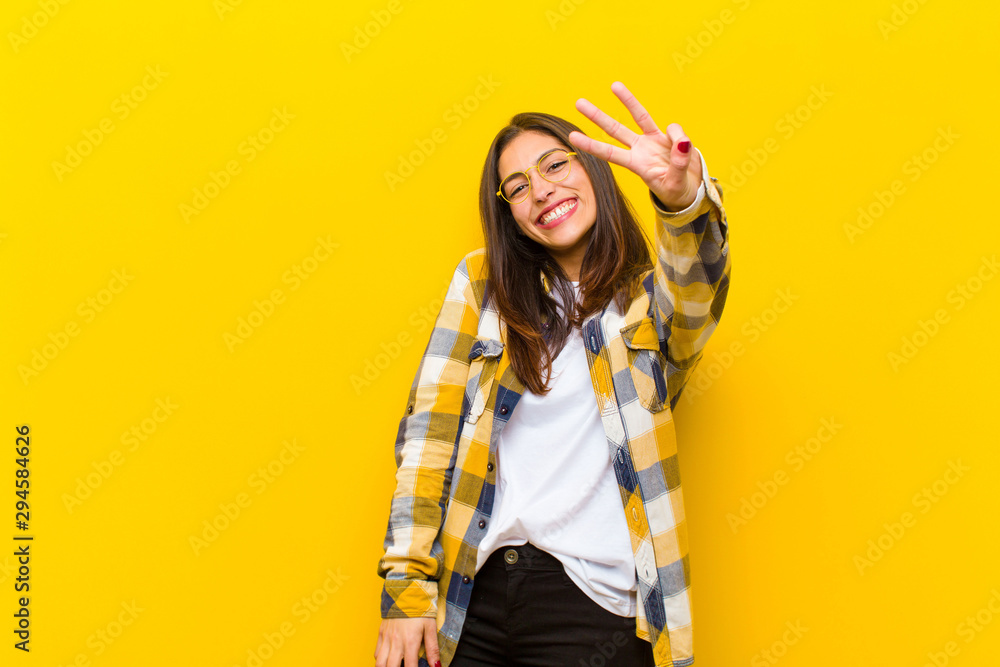 © kues1 - young  pretty woman smiling and looking friendly, showing number three or third with hand forward, counting down against orange wall