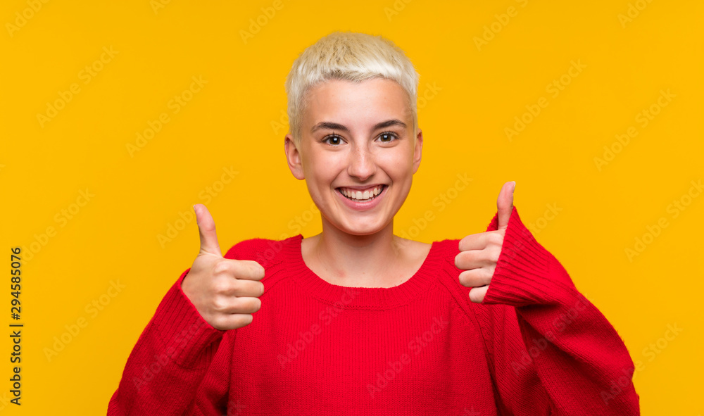 Teenager girl with white short hair over yellow wall giving a thumbs up gesture