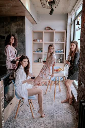 Multi ethnic ladies in amazing stylish pajamas enjoy the time together in a modern apartment design holding glasses of wine