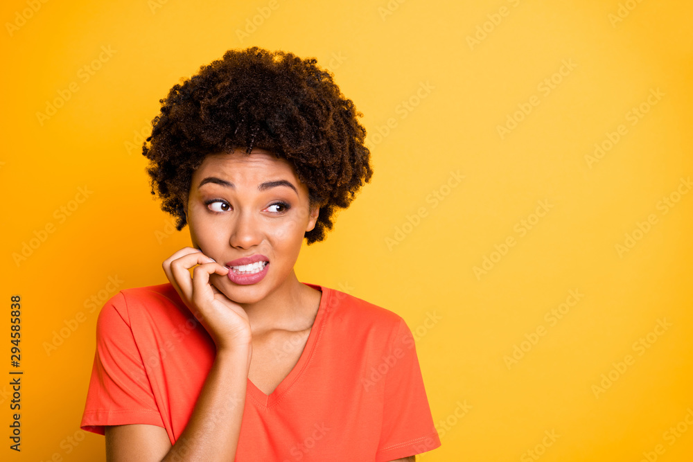 Copyspace photo of frightened afraid fearful woman biting her nails while observing terrible stuff going on wearing orange t-shirt isolated over yellow vivid color background Copyspace photo of frightened afraid fearful woman biting her nails while observing terrible stuff going on wearing orange t-shirt isolated over yellow vivid color background