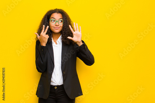 black business woman smiling and looking friendly, showing number eight or eighth with hand forward, counting down against orange wall photo