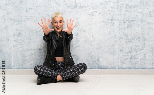 Young woman sitting on the floor counting nine with fingers photo