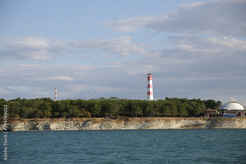 lighthouse on coast of sea. White and red color lighthouse. Against the blue sky. View from the sea.