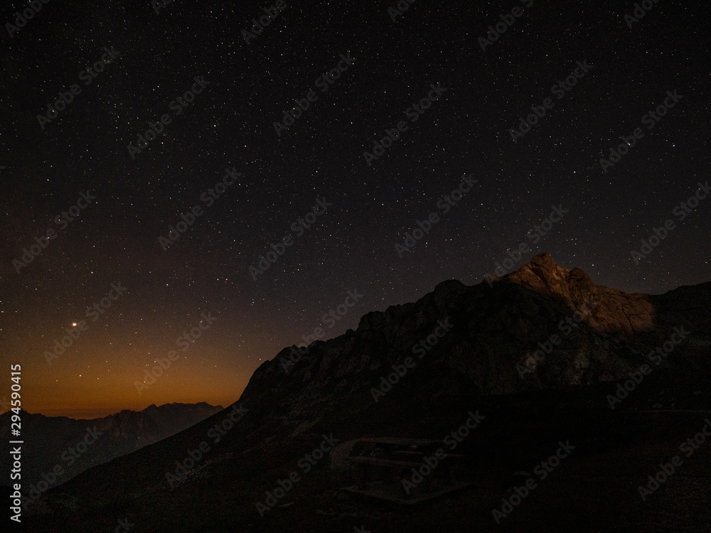 Sunset barely illuminates rocky mountaintop under the starry sky in Julian Alps.