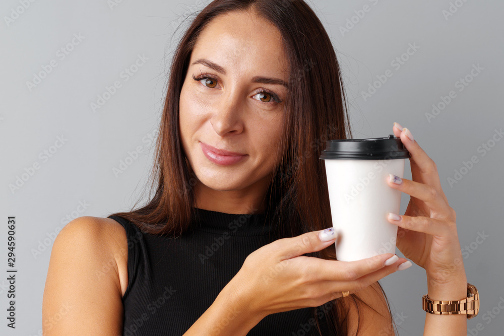 Nice brunette young woman holding a cup of coffee over a gray background. Nice brunette young woman holding a cup of coffee over a gray background.