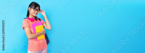 Young Asian girl student with school bag touching glasses isolated on blue background in studio, learning and education kid concept