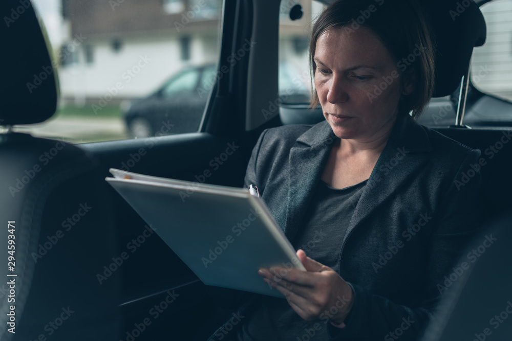 Businesswoman doing paperwork in car at the back seat