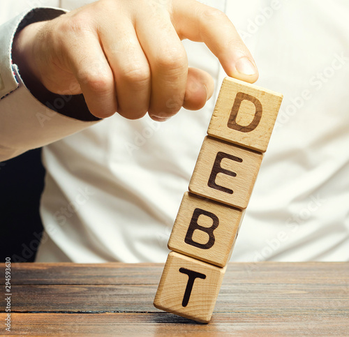 Businessman removes wooden blocks with the word Debt. Debt relief or cancellation is the partial or total forgiveness of debts, or the slowing or stopping growth. Restructuring. Pay. Redemption
