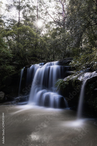 Waterfall view under the tree with sunlight piercing through.