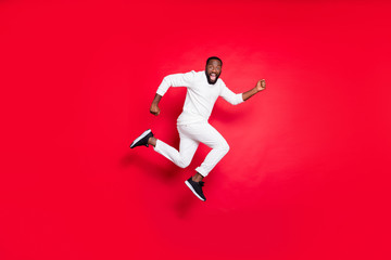 Full length profile photo of excited dark skin guy jumping high running x-mas shopping need buy many presents wear white sweater trousers isolated red background