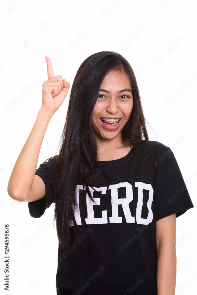 Studio shot of young happy Asian teenage nerd girl smiling while Studio shot of young happy Asian teenage nerd girl smiling while