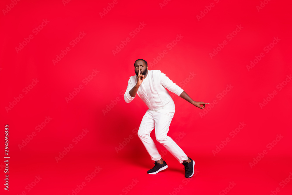 Full size photo of funny dark skin man making newyear surprise for girlfriend going tiptoe hold finger on lips wear knitted sweater trousers isolated red background Full size photo of funny dark skin man making newyear surprise for girlfriend going tiptoe hold finger on lips wear knitted sweater trousers isolated red background
