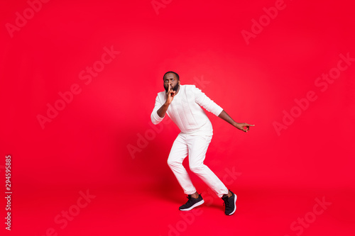 Full size photo of funny dark skin man making newyear surprise for girlfriend going tiptoe hold finger on lips wear knitted sweater trousers isolated red background photo
