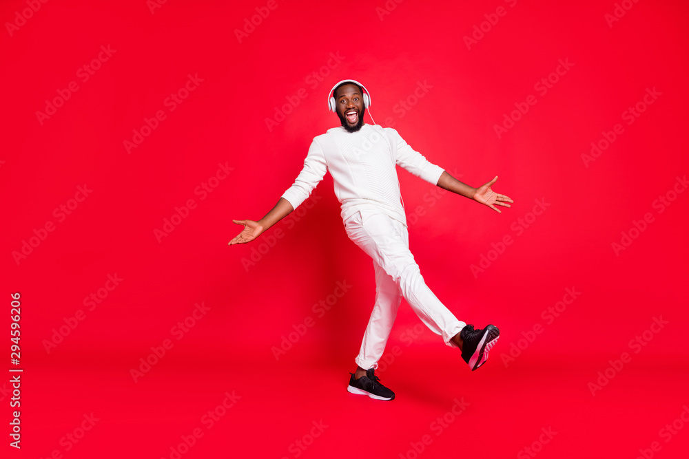 Full body photo of amazing dark skin man listening favorite playlist in earflaps moving with rhythm down street wear knitted sweater trousers isolated red background