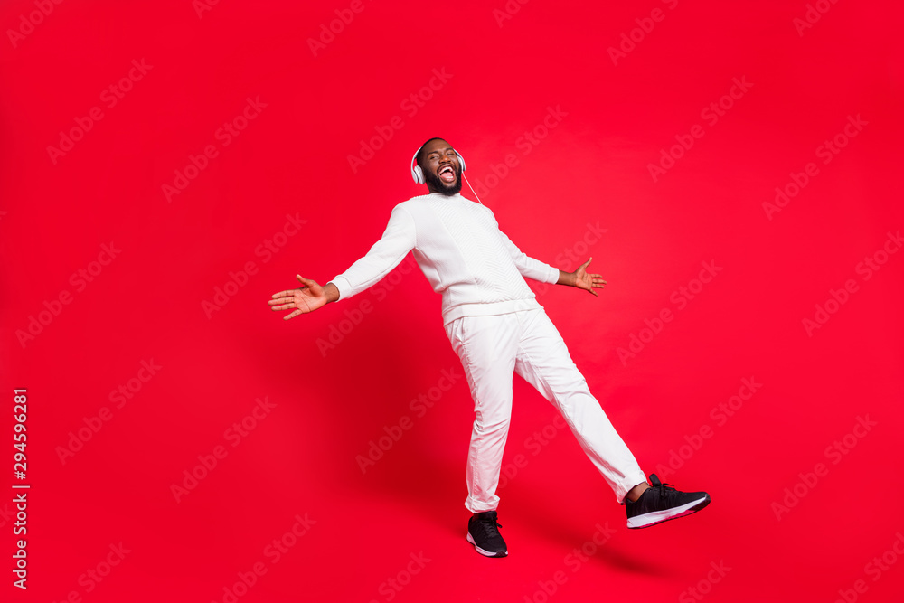 Full length photo of amazing dark skin man listening favorite playlist in earflaps enjoy best moment moving with rhythm wear knitted sweater and trousers isolated red background