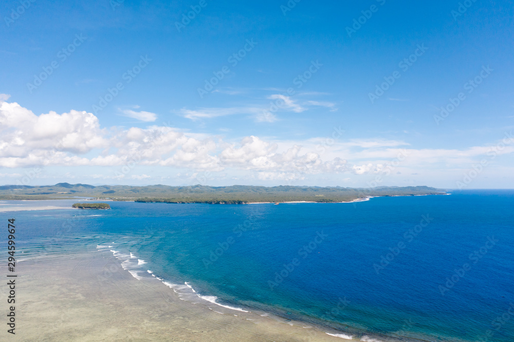 Seascape, coast of the island of Siargao, Philippines. Blue sea with waves and sky with big clouds, top view.