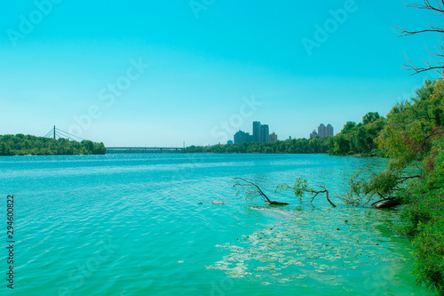 Wide river with green water with algae. River and foggy city with a bridge on the horizon