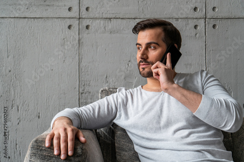 Handsome and stylish bearded businessman in casual clothes talking on smartphone sitting in armchair in loft office or at home. Concept of business lifestyle photo