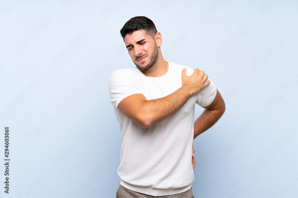 Caucasian handsome man over isolated blue background suffering from pain in shoulder for having made an effort Caucasian handsome man over isolated blue background suffering from pain in shoulder for having made an effort