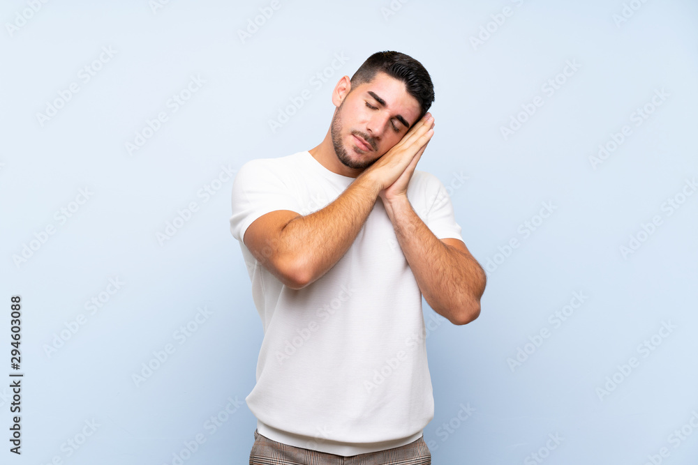 Caucasian handsome man over isolated blue background making sleep gesture in dorable expression Caucasian handsome man over isolated blue background making sleep gesture in dorable expression