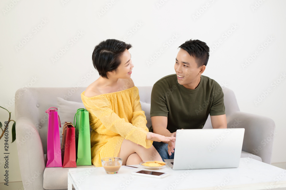 Young Couple Shopping Online On Laptop With Multi Colored Shopping Bags On Sofa Young Couple Shopping Online On Laptop With Multi Colored Shopping Bags On Sofa
