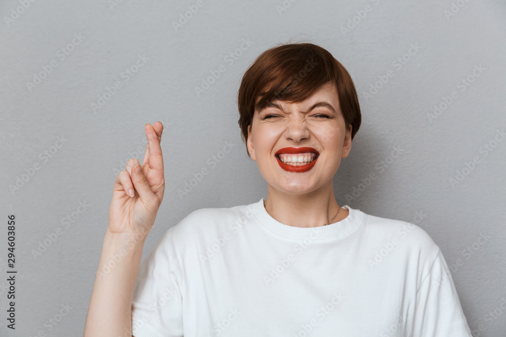 Image of happy brunette woman wearing casual t-shirt keeping fingers crossed Image of happy brunette woman wearing casual t-shirt keeping fingers crossed