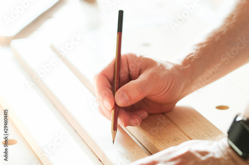 A carpenter applies marking with a pencil on a wooden block.