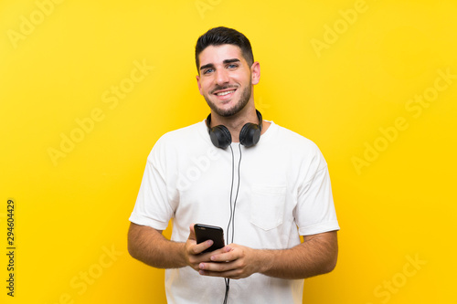 Young handsome man listening music with a mobile over isolated yellow wall