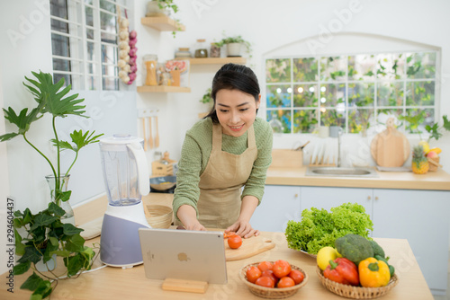Woman cutting vegetables in kitchen while watching tablet in front of her