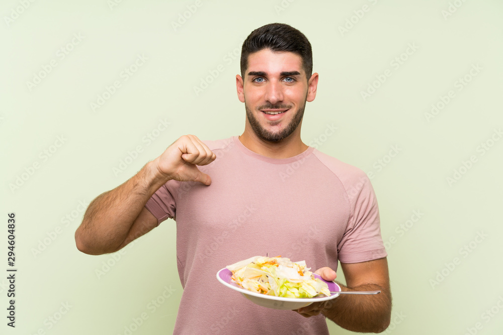 Young handsome man with salad over isolated green wall proud and self-satisfied Young handsome man with salad over isolated green wall proud and self-satisfied