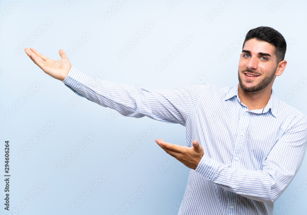 Caucasian handsome man over isolated blue background extending hands to the side for inviting to come Caucasian handsome man over isolated blue background extending hands to the side for inviting to come