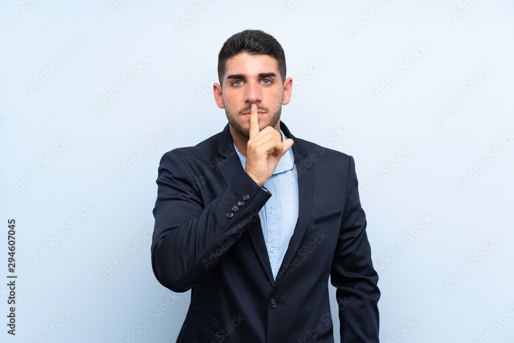 Handsome man over isolated blue background showing a sign of silence gesture putting finger in mouth Handsome man over isolated blue background showing a sign of silence gesture putting finger in mouth